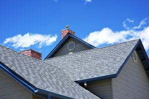 Asphalt shingle roof with blue trim and brick chimney under a clear blue sky