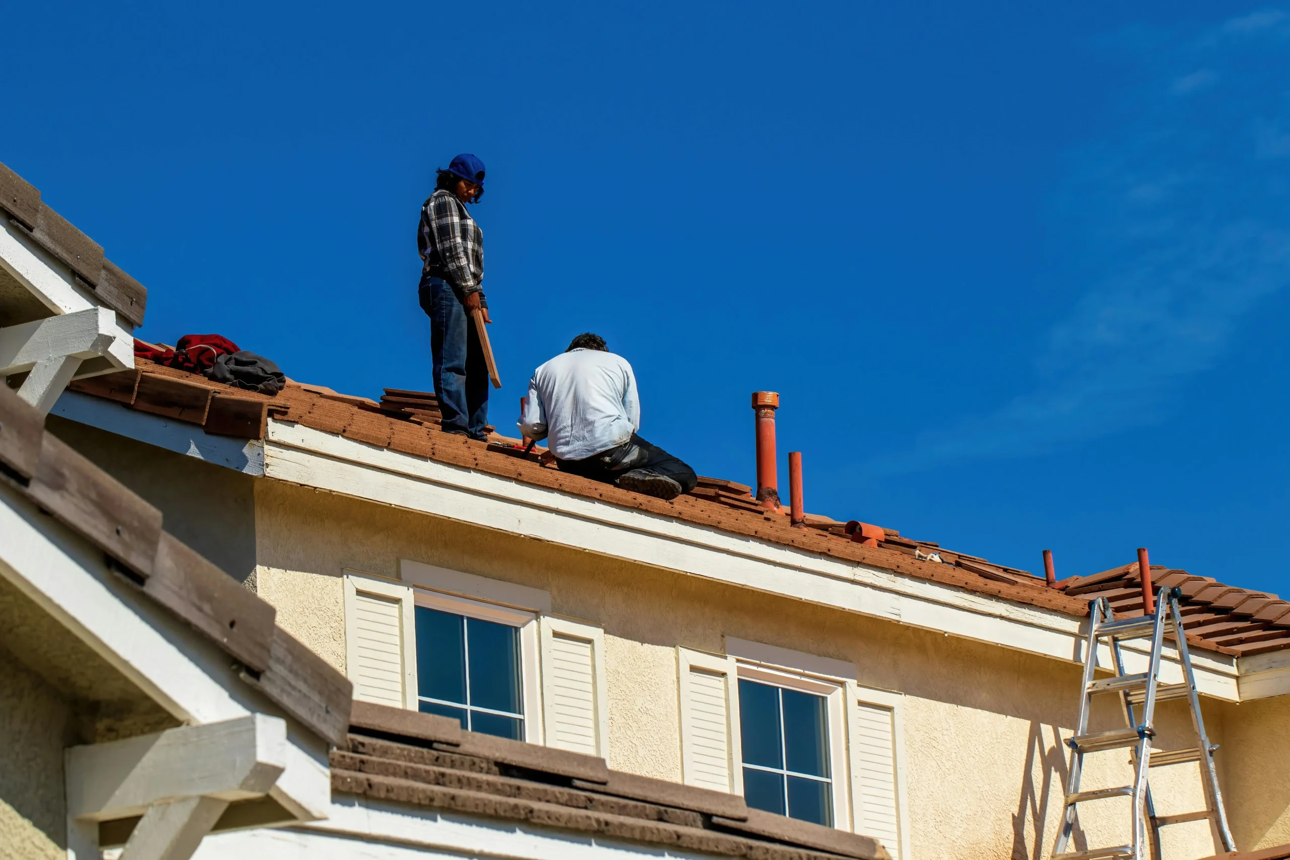 Two roofers working on a sloped shingle roof on a sunny day in Carrollton and the DFW area.