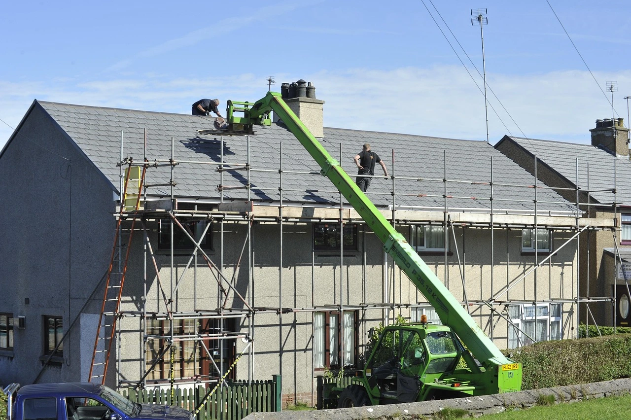 Roofers work on a residential roof using scaffolding and a boom lift on a clear day.