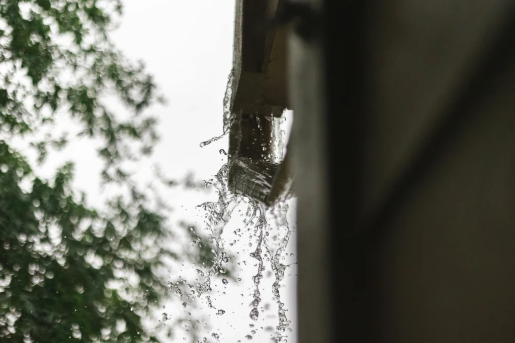 Rainwater overflows from a roof gutter and splashes down beside the house.