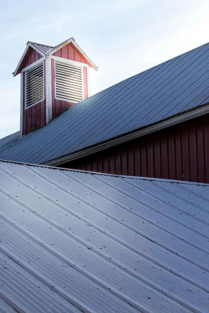 Metal roof on a barn with a small cupola vent against a bright sky.