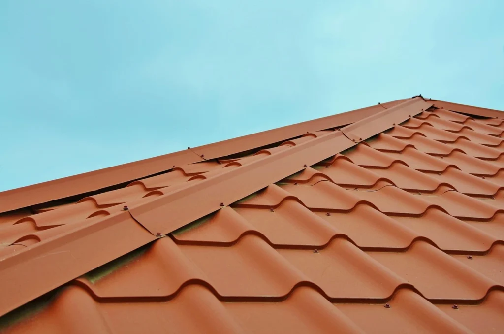 Close-up of a red metal roof ridge cap and fasteners against a clear sky.