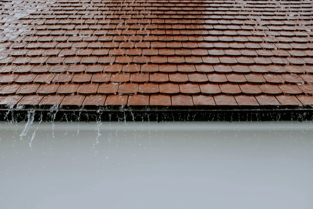 Rain falls on a shingle roof as water runs into the gutter along the eaves.