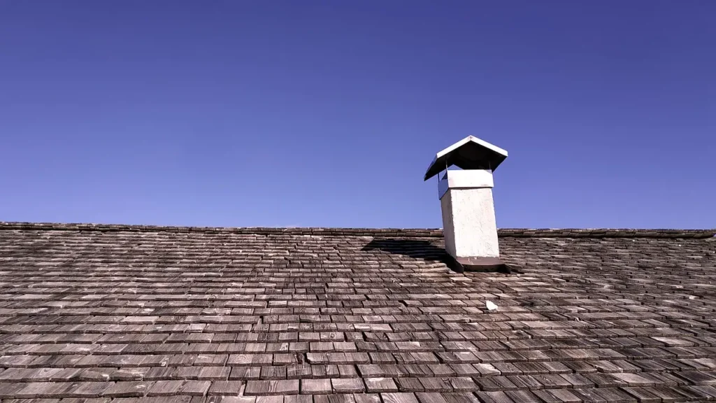 Shingle roof with a small vent stack and cap under a clear blue sky.
