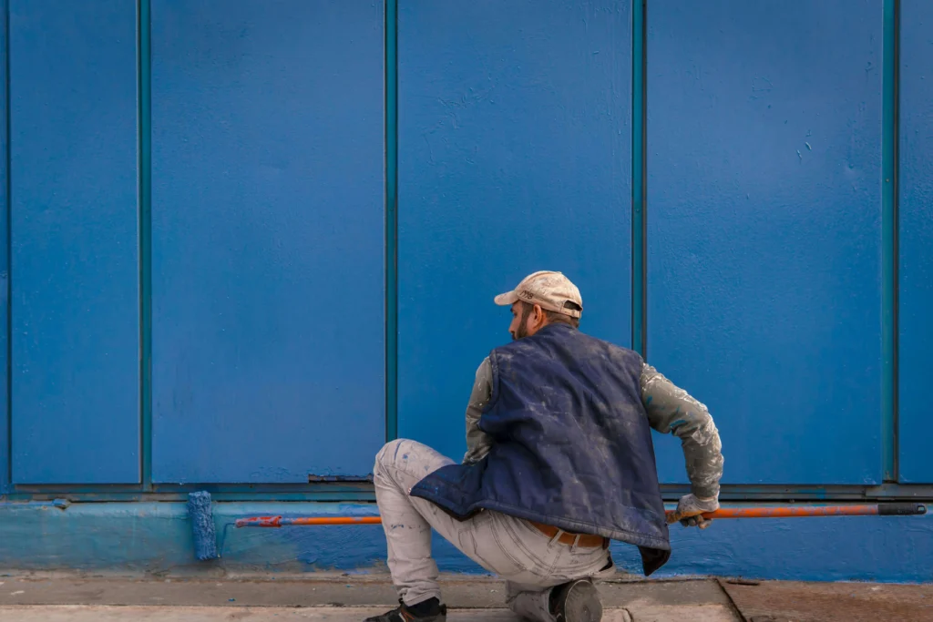 Contractor painting exterior wall with blue paint using roller during exterior painting project